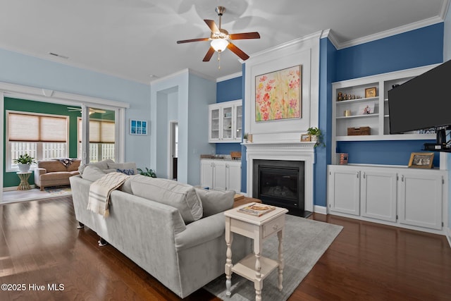 living room with crown molding, a ceiling fan, dark wood-type flooring, and a fireplace with flush hearth