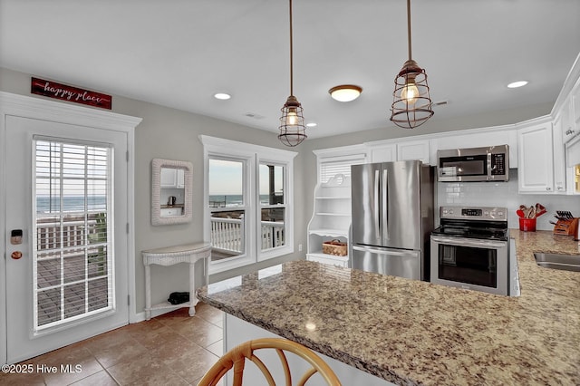 kitchen with a peninsula, light stone countertops, white cabinetry, and stainless steel appliances