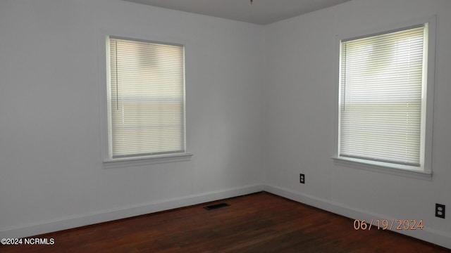 spare room featuring dark wood-style flooring, visible vents, and baseboards