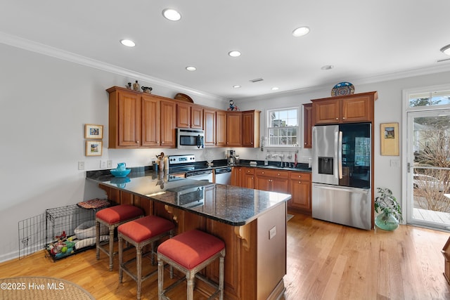 kitchen featuring brown cabinets, stainless steel appliances, light wood-style floors, a sink, and a peninsula