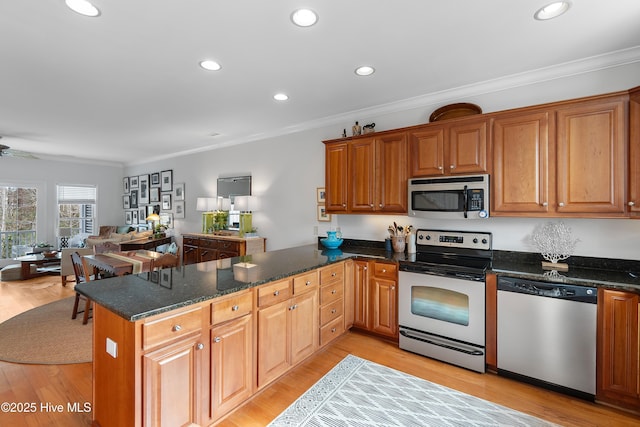 kitchen with appliances with stainless steel finishes, light wood-style floors, ornamental molding, and a peninsula