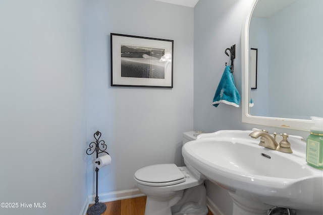 half bath featuring baseboards, a sink, toilet, and wood finished floors