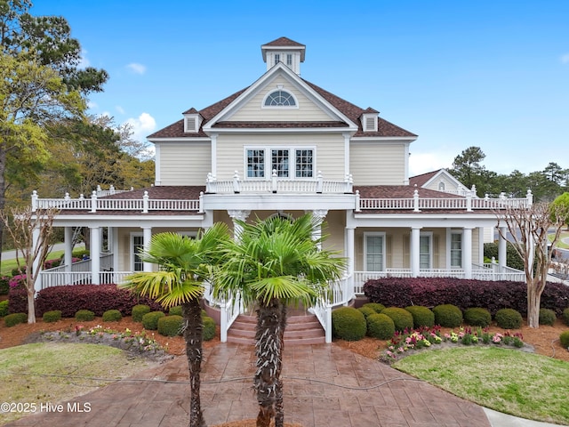view of front facade featuring a balcony, a shingled roof, a porch, and driveway