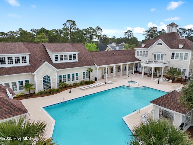 rear view of house featuring a community pool, a shingled roof, a hot tub, and a patio area