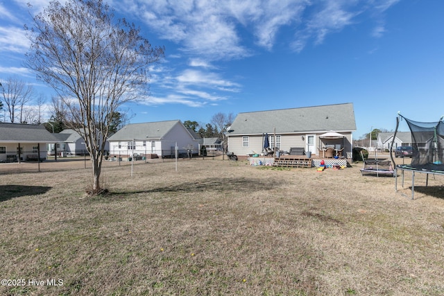 back of house featuring a yard, a trampoline, a wooden deck, and fence