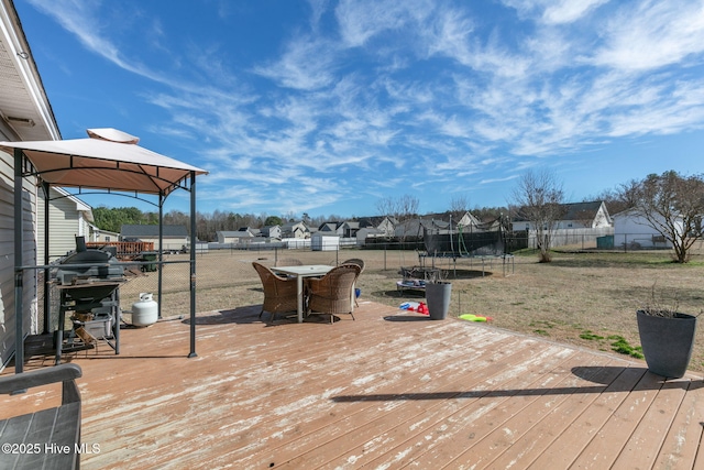 wooden terrace with a trampoline, a gazebo, a lawn, outdoor dining area, and a fenced backyard