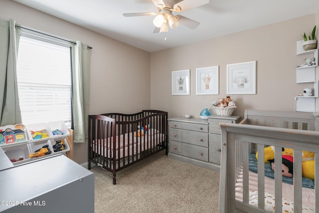 bedroom featuring ceiling fan, a nursery area, and light carpet