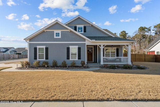 view of front of property with covered porch, roof with shingles, a front yard, and fence