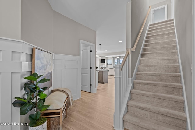 stairway featuring recessed lighting, a decorative wall, wood finished floors, and wainscoting