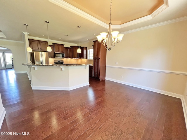 kitchen with dark wood-type flooring, a tray ceiling, appliances with stainless steel finishes, arched walkways, and a notable chandelier