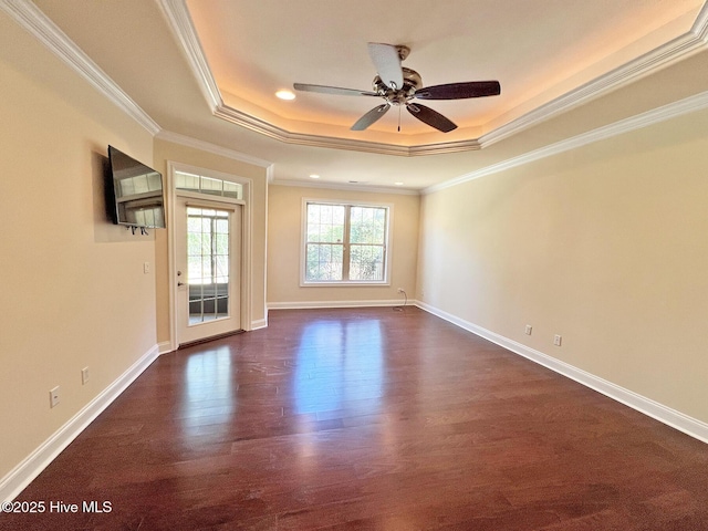 empty room with dark wood-type flooring, ceiling fan, baseboards, ornamental molding, and a raised ceiling