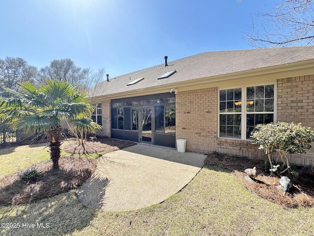 rear view of property with brick siding, a patio, and roof with shingles