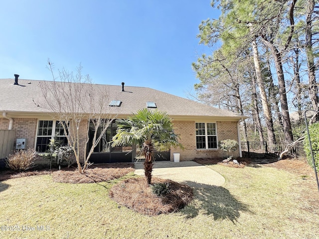 rear view of house featuring brick siding, a lawn, a shingled roof, and fence