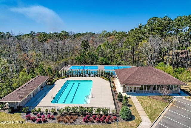 view of swimming pool with a patio, a fenced in pool, fence, a wooded view, and a lawn