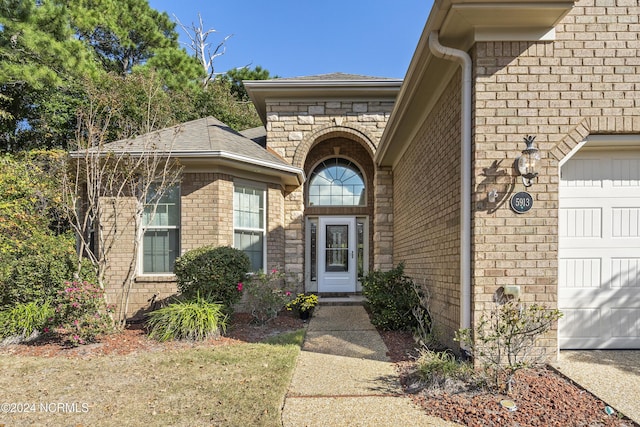 view of exterior entry with brick siding, a garage, and roof with shingles