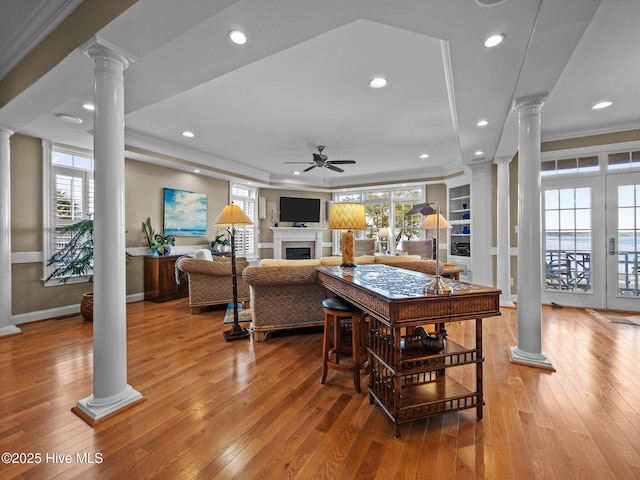 dining room with a ceiling fan, light wood-style flooring, ornamental molding, ornate columns, and a fireplace