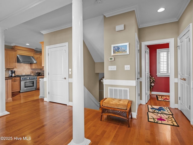 foyer with ornate columns, ornamental molding, and light wood finished floors