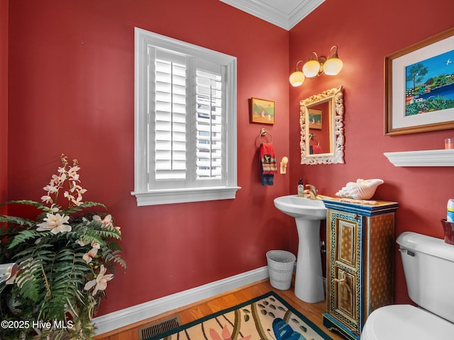 half bathroom featuring crown molding, visible vents, toilet, wood finished floors, and baseboards