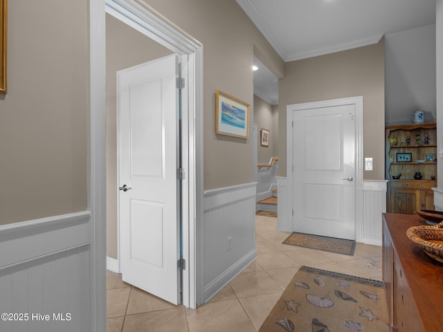 entryway with light tile patterned floors, a wainscoted wall, and crown molding