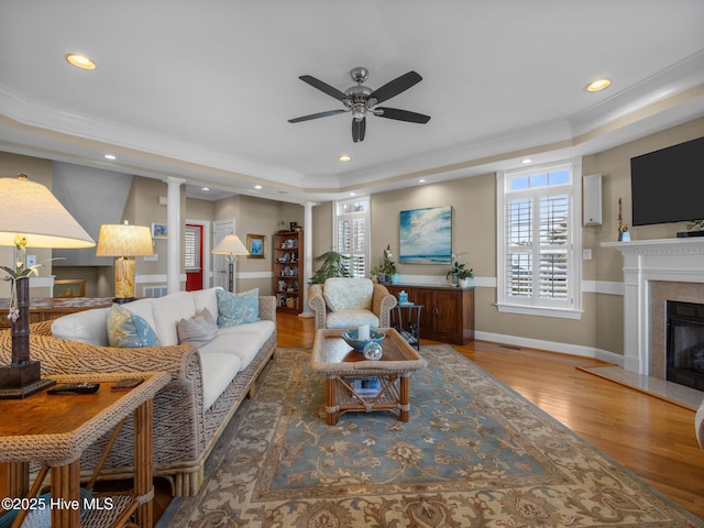 living area with recessed lighting, a raised ceiling, ornamental molding, a glass covered fireplace, and wood finished floors