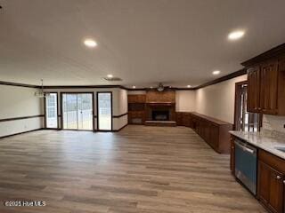 kitchen featuring a fireplace with raised hearth, light countertops, stainless steel dishwasher, crown molding, and open floor plan