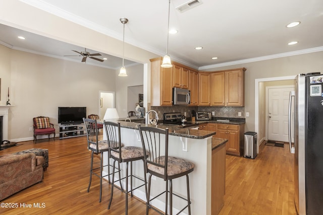 kitchen with visible vents, appliances with stainless steel finishes, open floor plan, a peninsula, and a kitchen bar