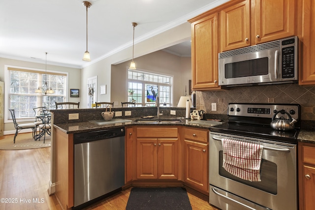 kitchen with light wood finished floors, appliances with stainless steel finishes, ornamental molding, a peninsula, and a sink