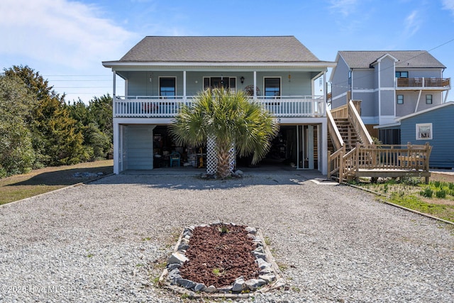 beach home featuring covered porch, a carport, roof with shingles, and gravel driveway