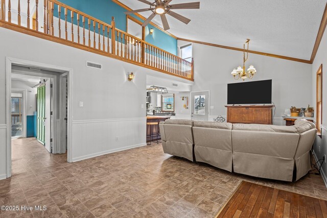 living area with vaulted ceiling, ceiling fan with notable chandelier, stairs, and crown molding