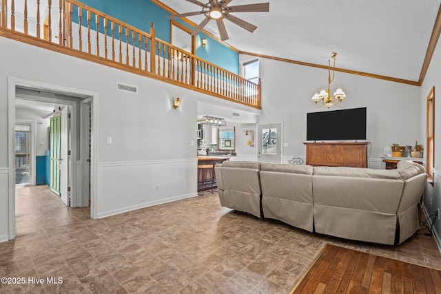 living area featuring ceiling fan with notable chandelier, vaulted ceiling, visible vents, and crown molding