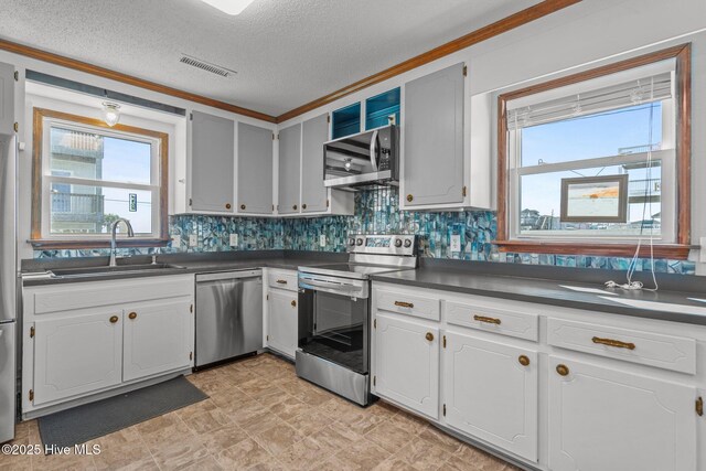 kitchen featuring visible vents, dark countertops, a sink, stainless steel appliances, and backsplash