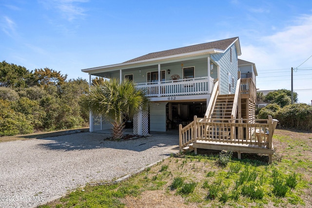 beach home featuring a porch, gravel driveway, a carport, and stairs