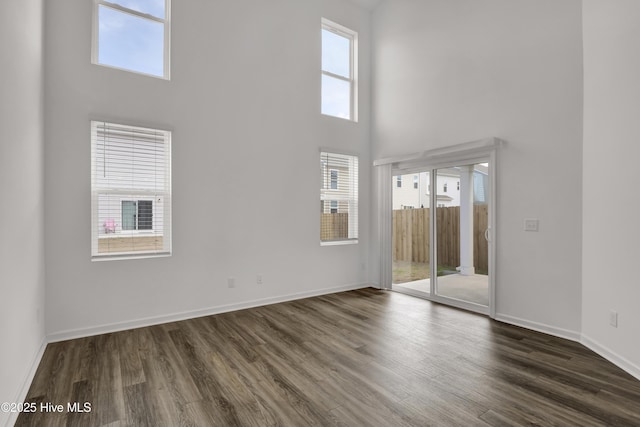 empty room with a high ceiling, dark wood-style flooring, and baseboards