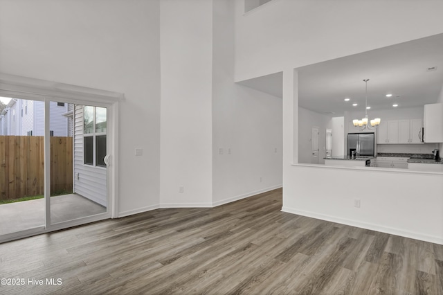 unfurnished living room with a notable chandelier, a towering ceiling, baseboards, and wood finished floors