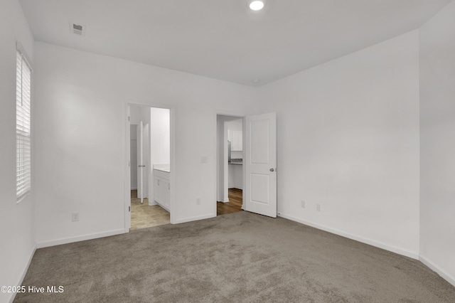 unfurnished bedroom featuring ensuite bath, carpet flooring, visible vents, and baseboards