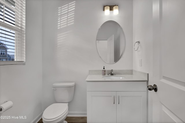 half bath featuring baseboards, a healthy amount of sunlight, vanity, and toilet