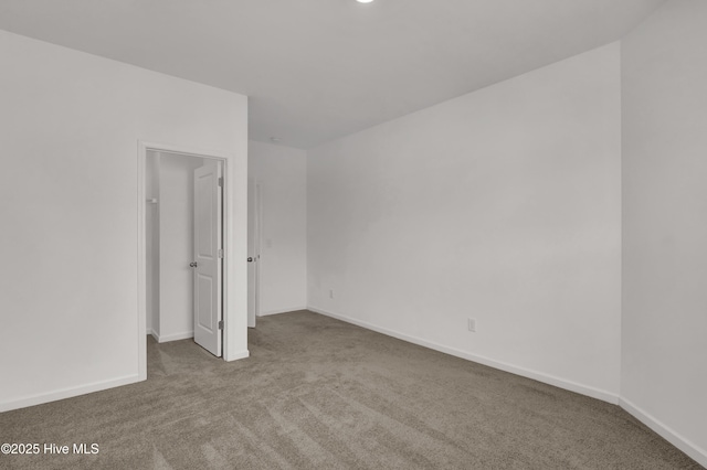 unfurnished bedroom featuring carpet floors, a spacious closet, and baseboards