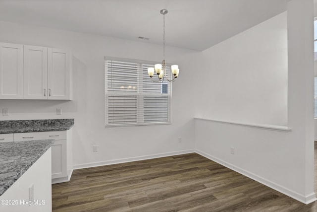 unfurnished dining area featuring dark wood-style flooring, an inviting chandelier, visible vents, and baseboards