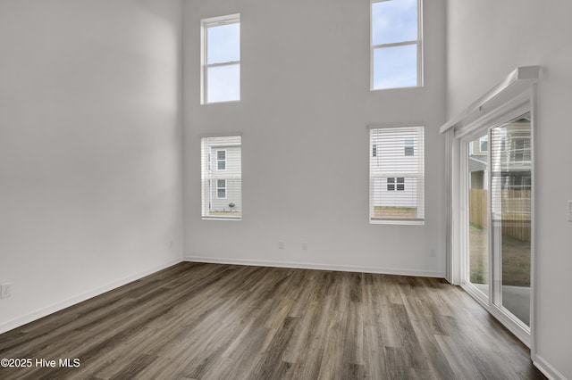 unfurnished living room featuring dark wood finished floors, a towering ceiling, and baseboards