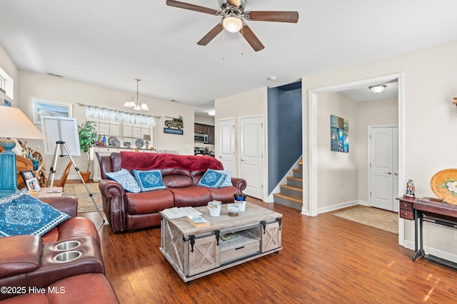 living area featuring ceiling fan with notable chandelier, stairway, baseboards, and wood finished floors