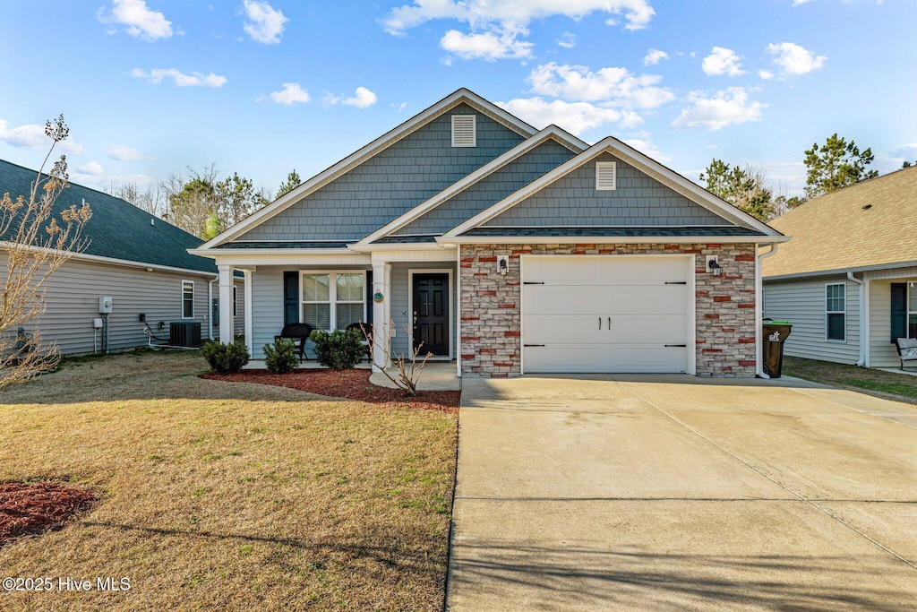 craftsman-style house featuring concrete driveway, an attached garage, covered porch, central air condition unit, and a front yard