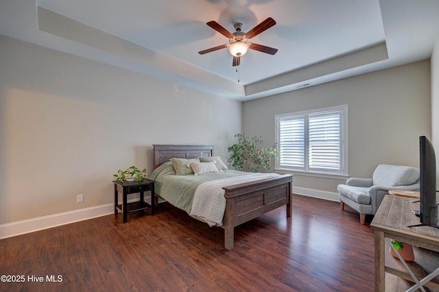 bedroom with baseboards, visible vents, dark wood-style floors, ceiling fan, and a tray ceiling