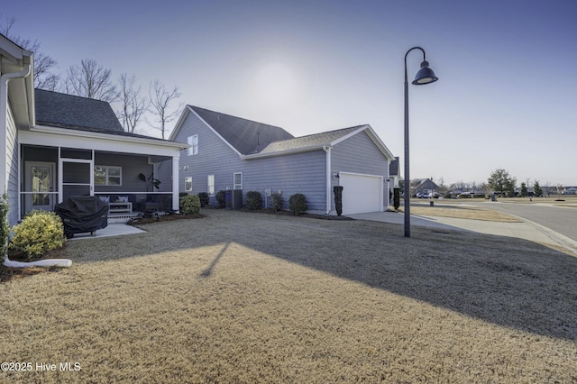 rear view of house with driveway, a sunroom, and roof with shingles