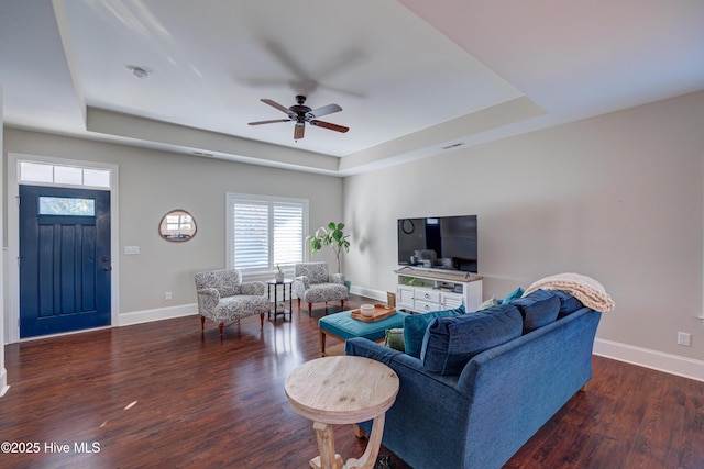 living area with a ceiling fan, baseboards, a tray ceiling, and wood finished floors