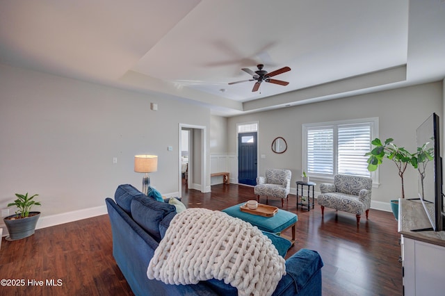 living area featuring a tray ceiling, ceiling fan, baseboards, and wood finished floors