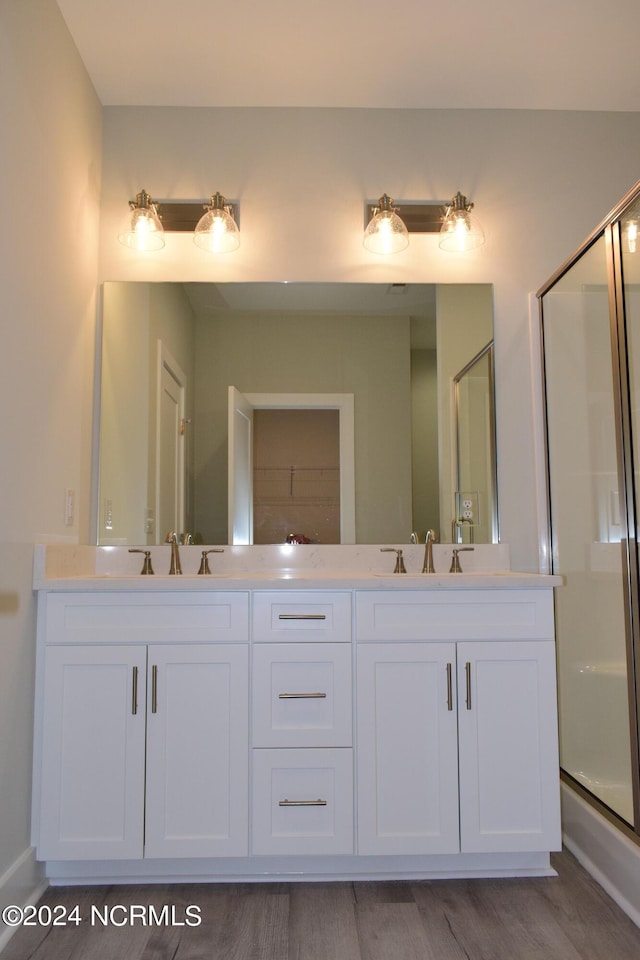 bathroom featuring double vanity, wood finished floors, a stall shower, and a sink