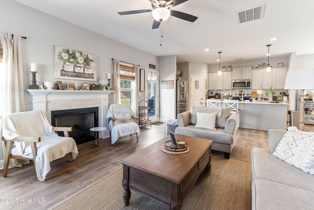 living room featuring ceiling fan, recessed lighting, a fireplace, visible vents, and light wood finished floors