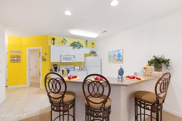 kitchen featuring recessed lighting, white cabinets, white appliances, a peninsula, and a kitchen breakfast bar