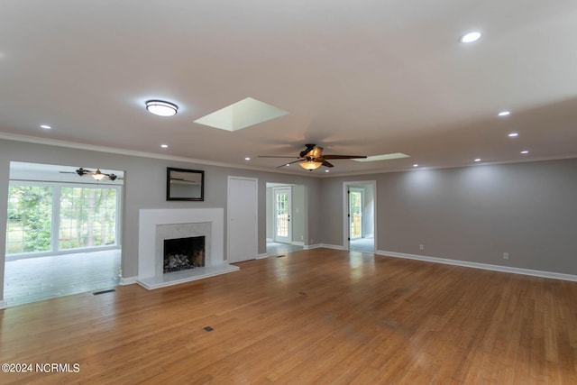 unfurnished living room with ornamental molding, a premium fireplace, a skylight, and wood finished floors