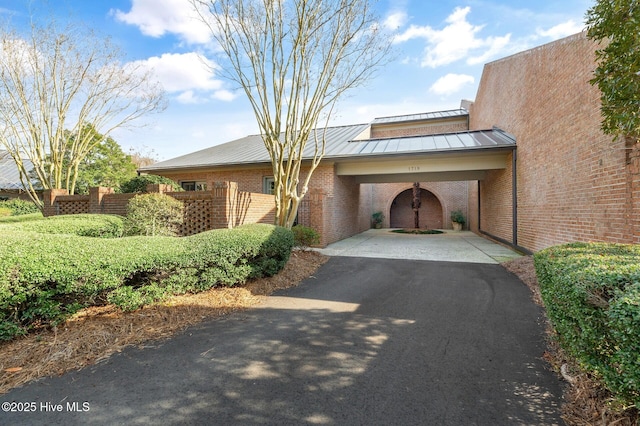 view of front of house featuring metal roof, an attached carport, aphalt driveway, brick siding, and a standing seam roof